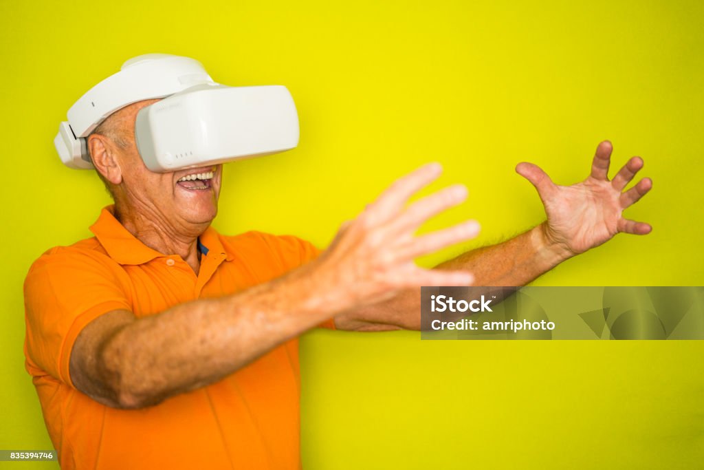 Color Surge for Stylish Seniors - senior man with VR googles and outstretched arms senior man 70 years old wearing 360 virtual reality 360vr goggles with orange shirt in vr color surge theme on colorful green background Virtual Reality Stock Photo