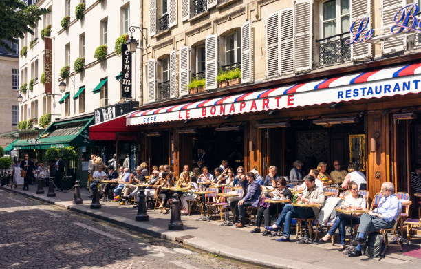 Parisian Cafe Paris, France - People sitting down to relax and enjoy food and drink at tables outside Le Bonaparte cafe in the St Germain district of central Paris. cafe culture stock pictures, royalty-free photos & images