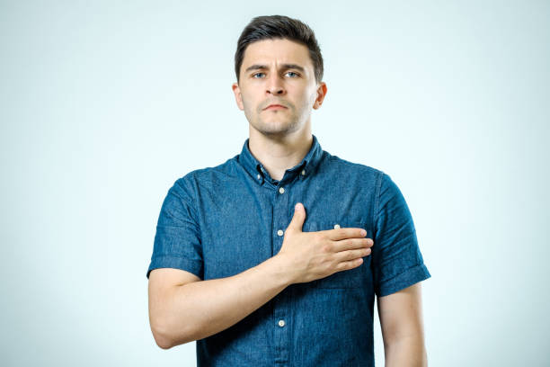 Young guy with his hand on his chest isolated on gray background