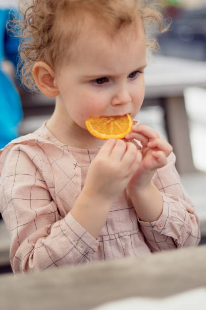 istock A little girl with curly hair eats an orange. 835452926