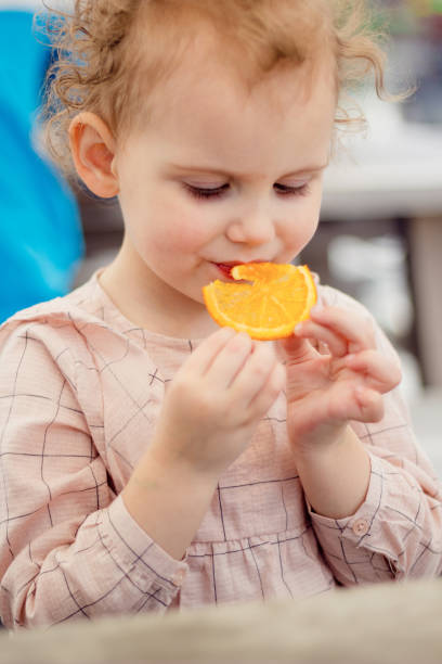 istock A little girl with curly hair eats an orange. 835452936