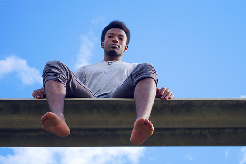 young african man sitting blue sky gray t-shirt low angle view