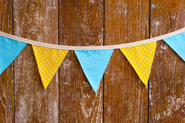 istock Triangular yellow and blue flag hanging with rope on brown wooden wall. can use for special occasion or party concept. 835524426