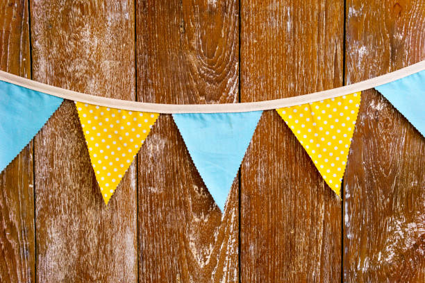 istock Triangular yellow and blue flag hanging with rope on brown wooden wall. can use for special occasion or party concept. 835524438