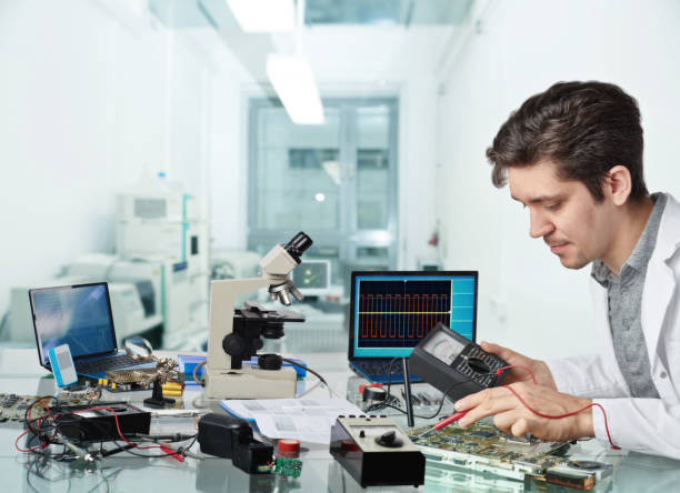 Young energetic male tech or engineer repairs electronic equipment in research facility. Shallow DOF, focus on the face of the worker.