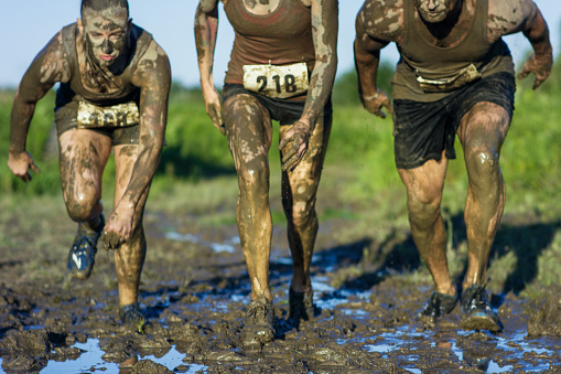 A small group of people are participating in a mud run for a charity. They are running together while covered in mud and wearing marathon numbers.
