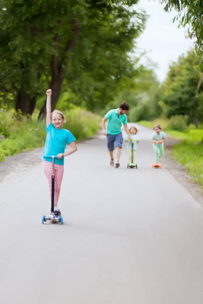 istock Father and three daughters at the walk, riding scooters 835593116