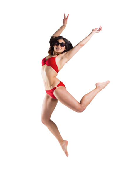 Fit girl in red bikini smiling and leaping on white background