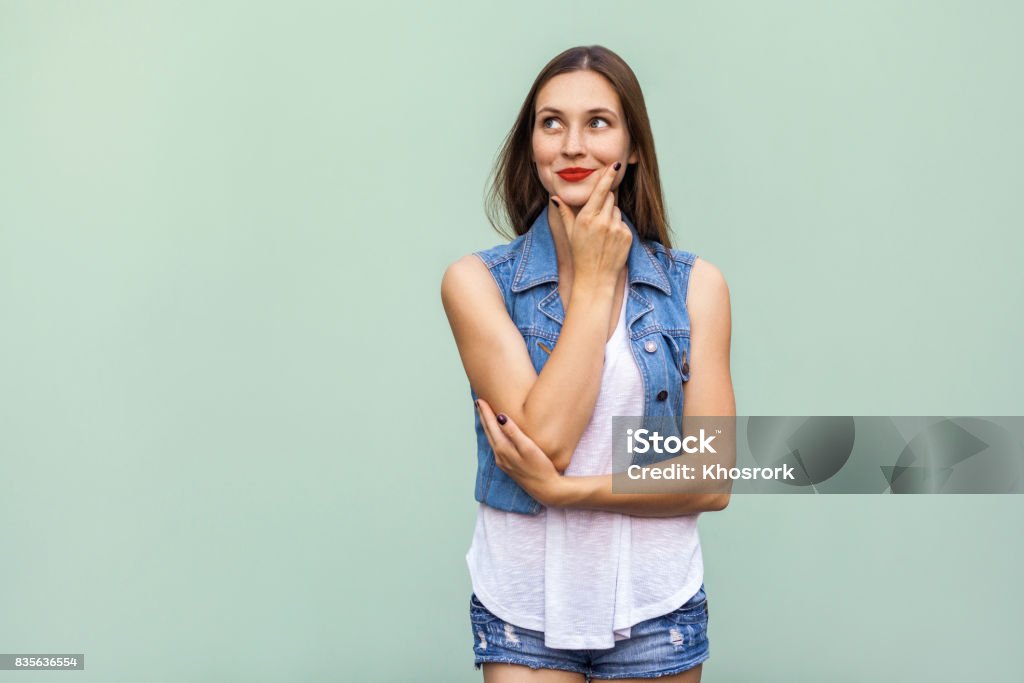 Joyeux joyeuse adolescente avec taches de rousseur, style décontracté blanc veste t shirt et jeans, levant, de penser et de toucher son visage et bénéficiant d’un, bon jour et gratuit le temps à l’intérieur. Studio, coup, fond vert clair - Photo de Femmes libre de droits