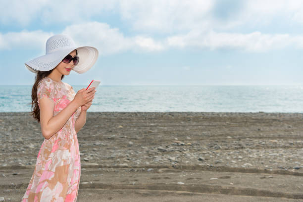 istock girl standing on the beach using the mobile 835659390