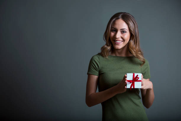 Cute happy female with a wrapped gift on grey background stock photo
