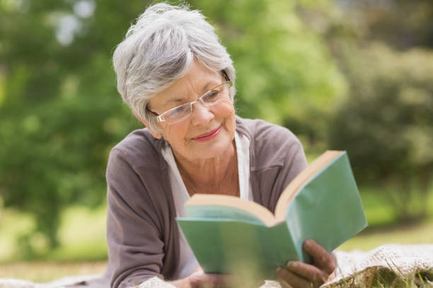 donna anziana che legge un libro al parco - people joy relaxation concentration foto e immagini stock