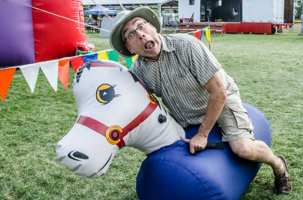 Man riding an inflatable horse and falling on the ground during ther race in summer fair during day