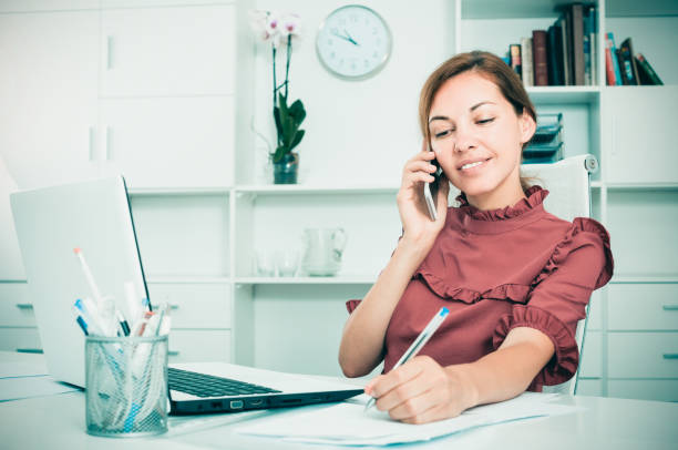 istock attentive female employee answering on phone and taking notes 835732836
