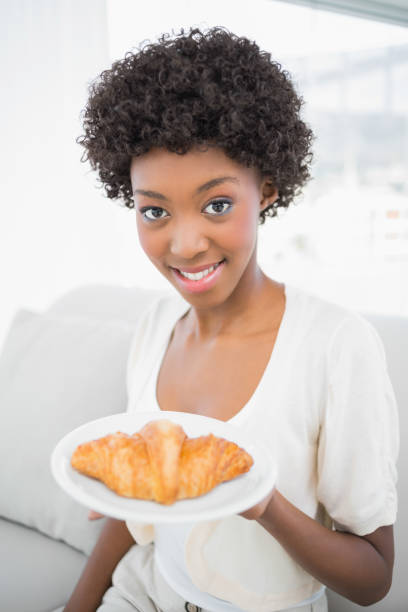 Happy gorgeous brunette having croissant for breakfast sitting on cosy sofa