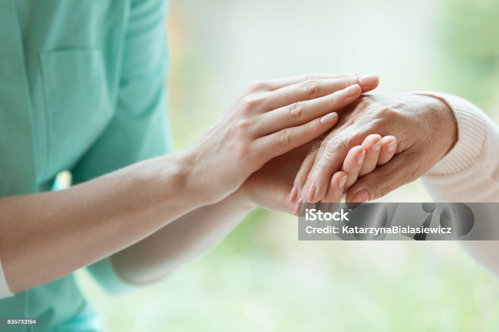 Caretaker massaging pensioner's hand Young caretaker massaging pensioner's hand with Parkinson's disease Hospice Stock Photo