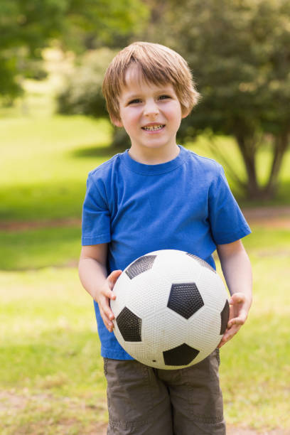istock Smiling young boy holding ball in park 835743512