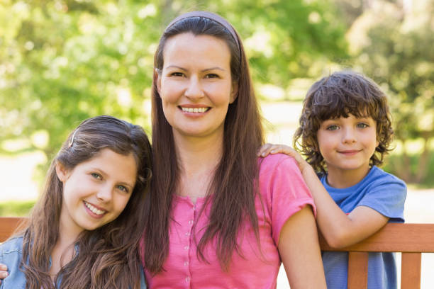 istock Smiling woman with kids sitting on park bench 835754890