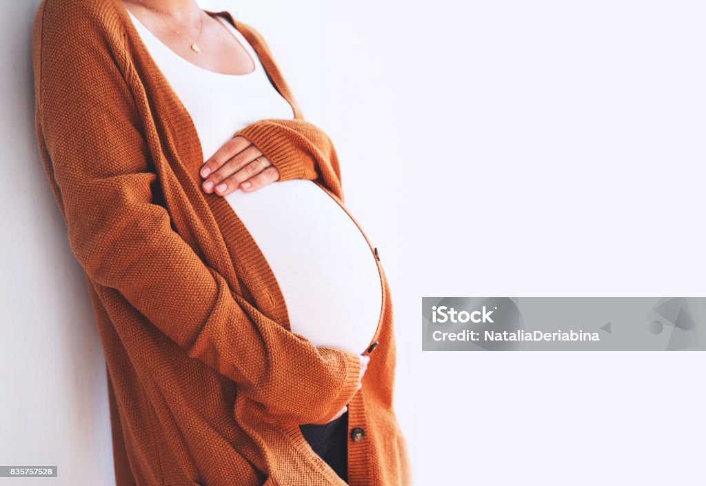 Beautiful pregnant woman touching her belly with hands on a white background. Beautiful pregnant woman touching her belly with hands on a white background. Young mother anticipation of the baby. Image of pregnancy and maternity. Close-up, copy space, indoors. Maternity wear Pregnant Stock Photo