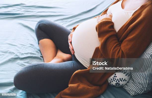 Schöne Schwangere Frau Sitzen Am Bett Und Hält Die Hände Auf Den Bauch Im Schlafzimmer Zu Hause Stockfoto und mehr Bilder von Schwanger