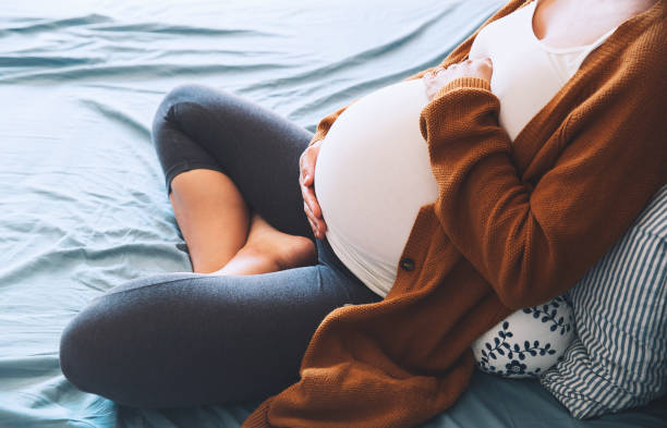 hermosa mujer embarazada sentada en cama y tiene las manos en el vientre en el dormitorio en el hogar. - abdomen humano fotografías e imágenes de stock