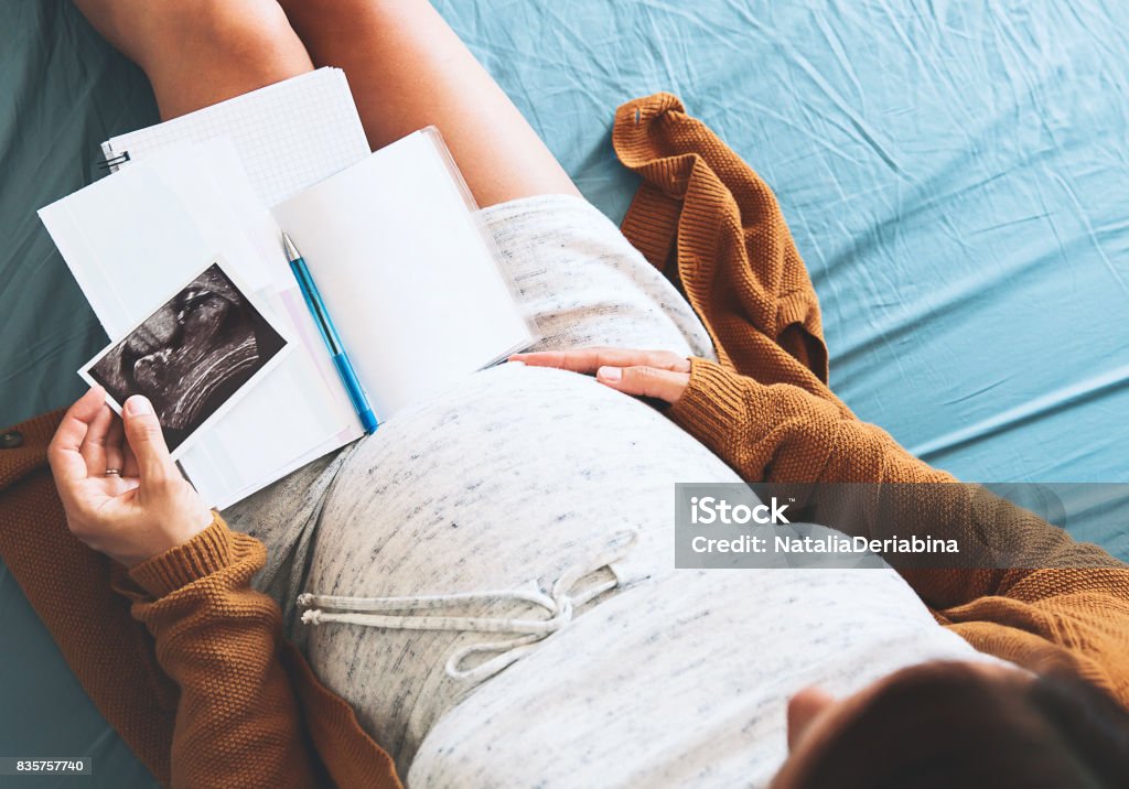 Mujer embarazada hace notas, mirando la imagen de ultrasonido y documentos médicos. - Foto de stock de Feto - Etapa humana libre de derechos