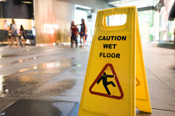 Caution wet floor, yellow warning sign stands on gray asphalt urban ground, close up photo