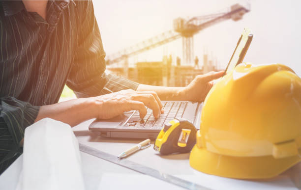 ingegnere architetto che utilizza laptop per lavorare con casco giallo, laptop e tazza di caffè sul tavolo. - computer construction using laptop construction site foto e immagini stock