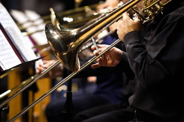 Trombones in the hands of musicians in the orchestra closeup in dark tones