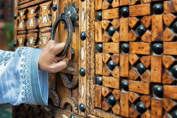 una mano che tiene una maniglia della porta di una tradizionale porta marocchina in legno. - gate handle door traditional culture foto e immagini stock