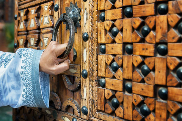 A hand holding a door handle of a traditional, wooden, moroccan door. stock photo