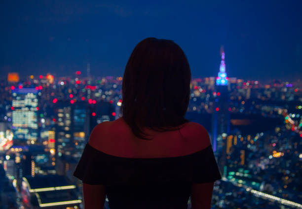 istock Girl looking through window upon city at night 835782928