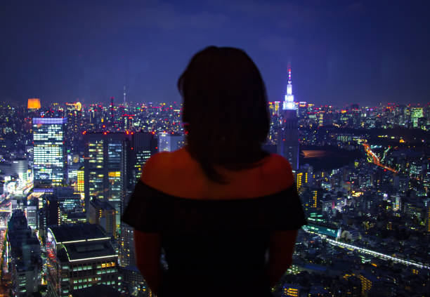 istock GIRL LOOKING THROUGH WINDOW UPON CITY AT NIGHT 835783358