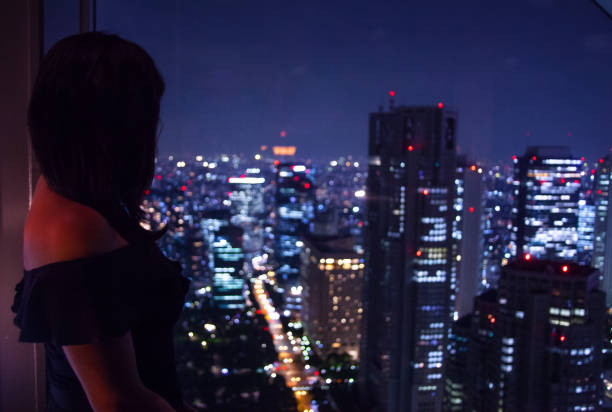 istock GIRL LOOKING THROUGH WINDOW UPON CITY AT NIGHT 835783362