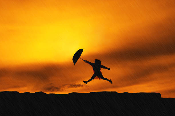 junges mädchen asiatische springen mit regenmantel und schirm am berg in der regenzeit-silhouette - happy men rain water dance stock-fotos und bilder