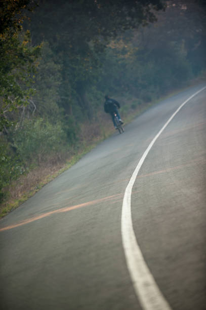 Road with solid middle line and cyclist A tilted arty photo of a tar road with a solid middle line going around a corner and a cyclist top left cycling out of focus Jonkershoek Stellenbosch Cape Town South Africa uci road world championships stock pictures, royalty-free photos & images