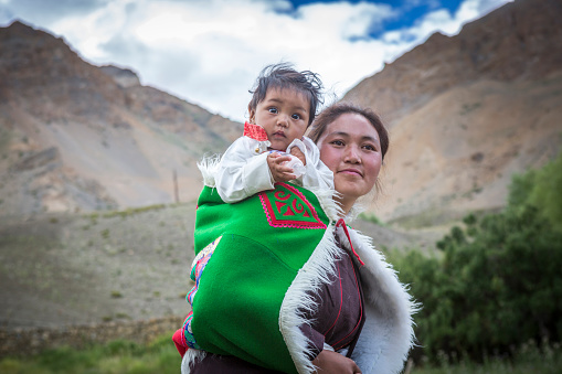 indian woman carrying baby on her back in traditional dress in spiti valley, india