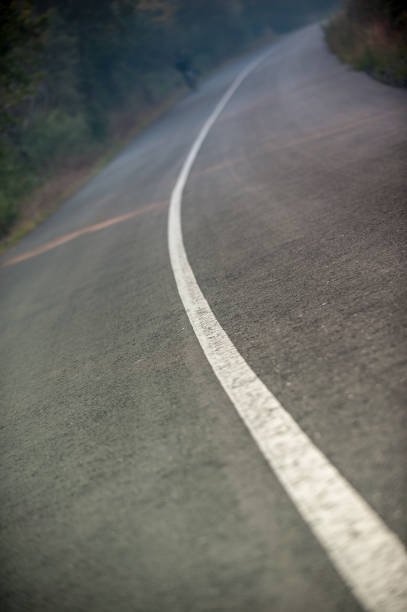 Road with solid middle line and cyclist A tilted arty photo of a tar road with a solid middle line going around a corner and a cyclist top left cycling out of focus Jonkershoek Stellenbosch Cape Town South Africa uci road world championships stock pictures, royalty-free photos & images