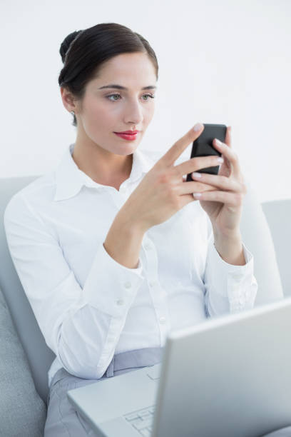 istock Well dressed woman using cellphone and laptop on sofa 835825168
