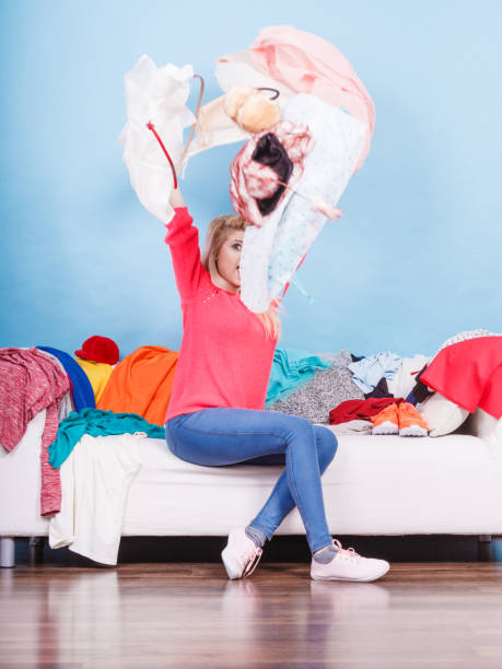 istock Woman sitting on messy couch throwing clothes 835829548