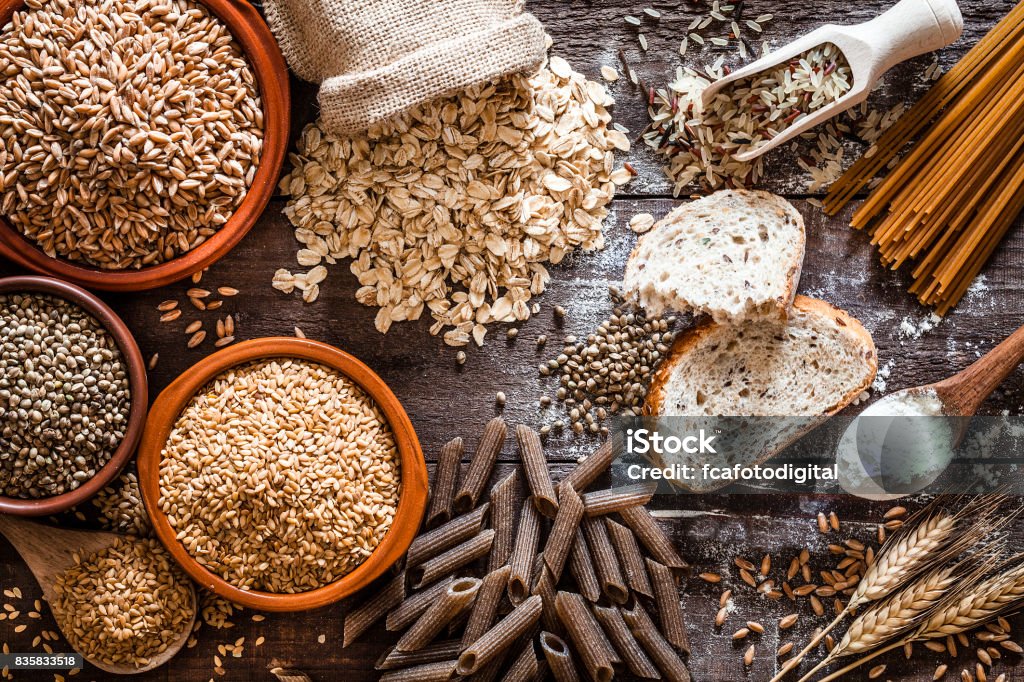 Wholegrain food still life shot on rustic wooden table Top view of wholegrain and cereal composition shot on rustic wooden table. This type of food is rich of fiber and is ideal for dieting. The composition includes wholegrain sliced bread, various kinds of wholegrain pasta, wholegrain crackers, grissini, oat flakes, brown rice, spelt and flax seeds. Predominant color is brown. DSRL studio photo taken with Canon EOS 5D Mk II and Canon EF 100mm f/2.8L Macro IS USM Wholegrain Stock Photo