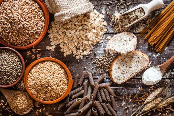 Wholegrain food still life shot on rustic wooden table Top view of wholegrain and cereal composition shot on rustic wooden table. This type of food is rich of fiber and is ideal for dieting. The composition includes wholegrain sliced bread, various kinds of wholegrain pasta, wholegrain crackers, grissini, oat flakes, brown rice, spelt and flax seeds. Predominant color is brown. DSRL studio photo taken with Canon EOS 5D Mk II and Canon EF 100mm f/2.8L Macro IS USM rice food staple stock pictures, royalty-free photos & images