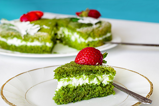 Green spinach cake with butter cream and strawberry on a white-gold plate. Selective focus