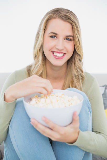 istock Cheerful pretty blonde eating popcorn sitting on cosy sofa 835838530