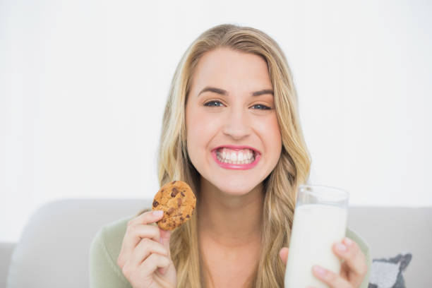 istock Happy cute blonde eating cookie with milk sitting on cosy sofa 835838698