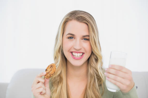 istock Smiling cute blonde eating cookie with milk sitting on cosy sofa 835838730