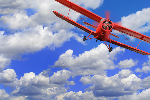 Red airplane biplane with piston engine flies and makes turn in cloudy sky