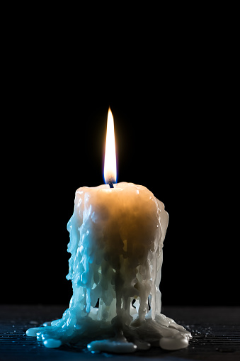 Single burning candle. Light of flame and flowing candle wax, dark background