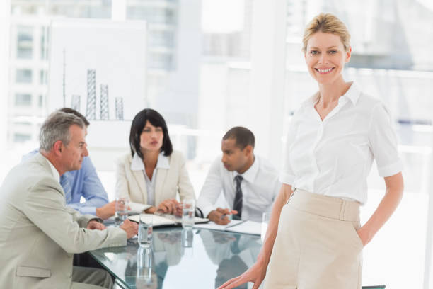 istock Happy businesswoman looking at camera while staff discuss behind her 835868158
