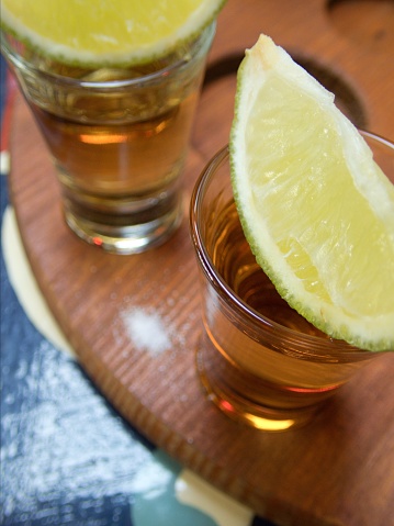 glasses with mexican mezcal tequila and slices of limes on wooden tray